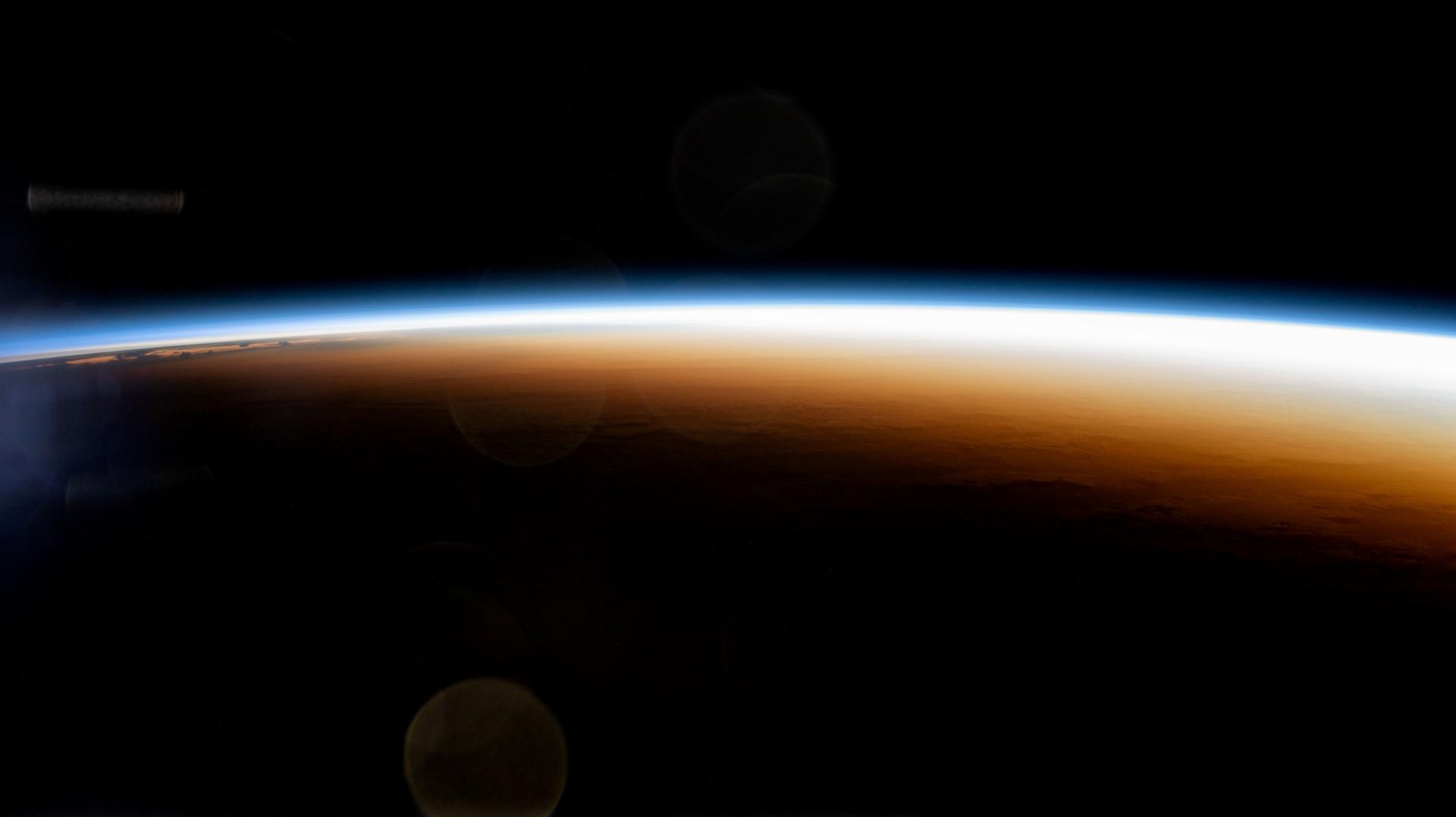 An orbital sunrise seen from low Earth orbit: a thin brilliant arc of sunlight along the curve of the planet against the black of space.