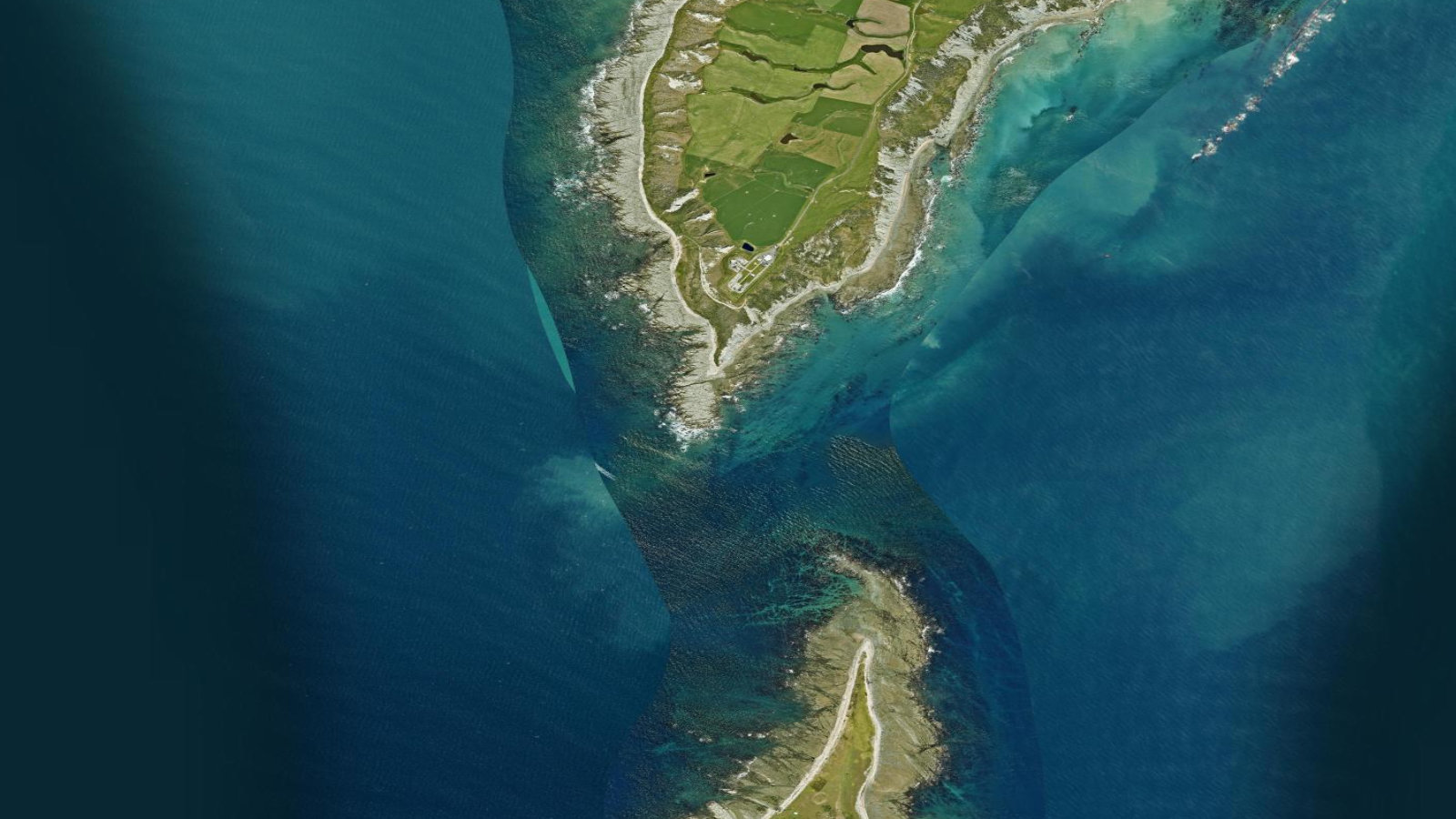 Satellite view of the tip of New Zealand's Māhia Peninsula, a green farmed headland ringed by reef and ocean, with a launch facility set near the shore.